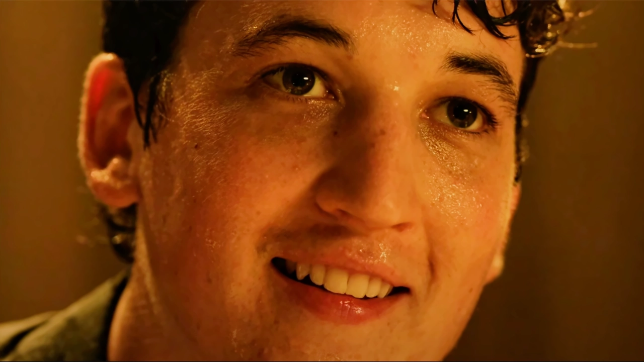 Primer plano de Andrew Neiman sudando y sonriendo satisfactoriamente durante el solo final de batería en Whiplash.