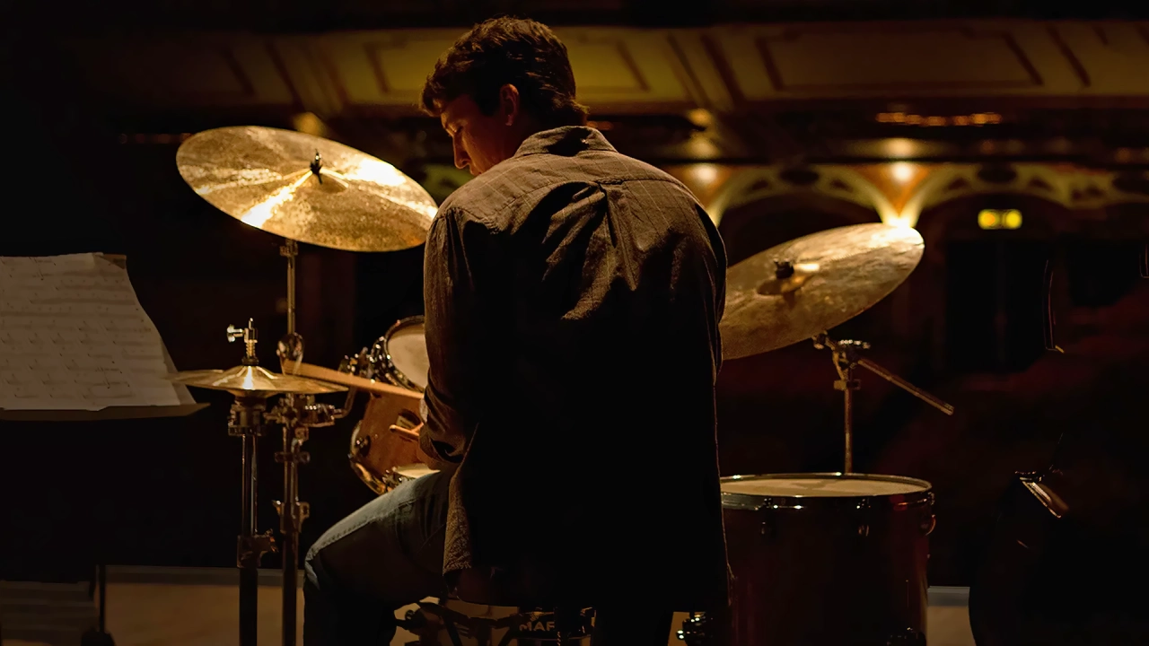 Andrew Neiman de espaldas tocando la batería solo en un escenario iluminado durante la película Whiplash.