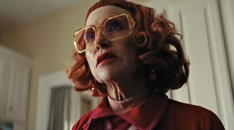 Primer plano desde abajo de Gladys, interpretada por Amy Madigan, con anteojos grandes y cabello rojo en la película de terror Weapons.