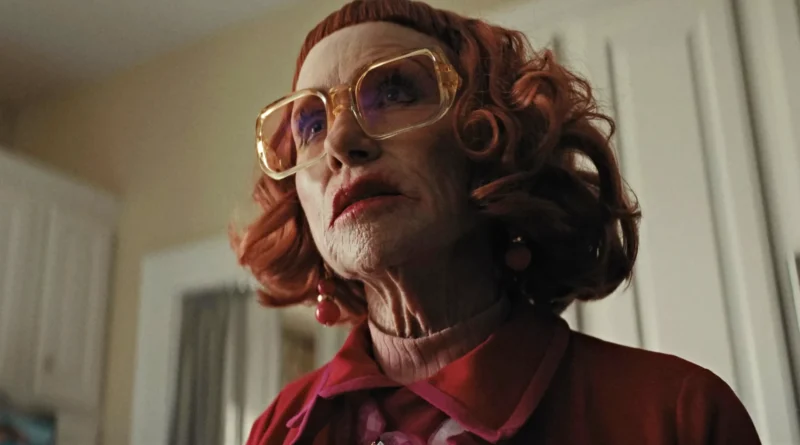 Primer plano desde abajo de Gladys, interpretada por Amy Madigan, con anteojos grandes y cabello rojo en la película de terror Weapons.