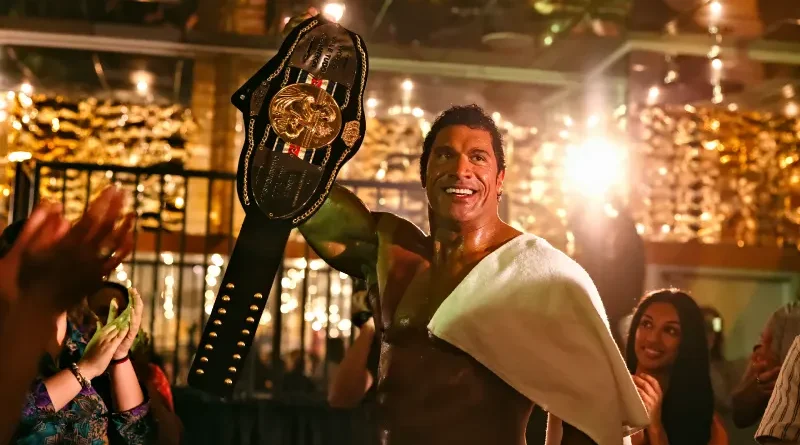 Dwayne Johnson como Mark Kerr sonriendo y levantando un cinturón de campeonato rodeado de gente en The Smashing Machine.
