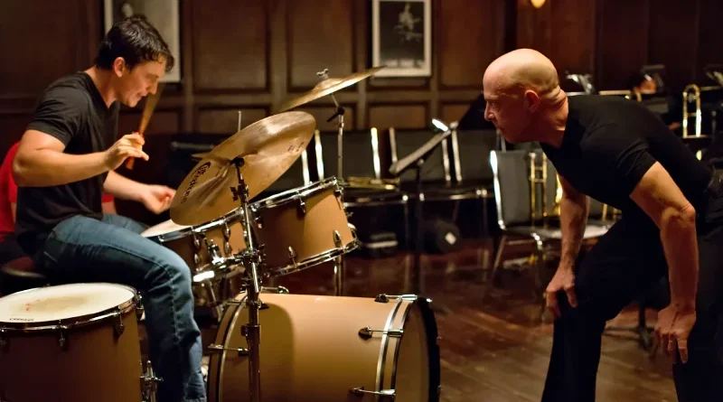 Andrew Neiman tocando la batería con esfuerzo mientras Terence Fletcher lo observa intensamente en un ensayo de Whiplash.